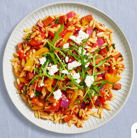 A plate of orzo with cherry tomatoes and tomato sauce dressed with goat cheese and rucola